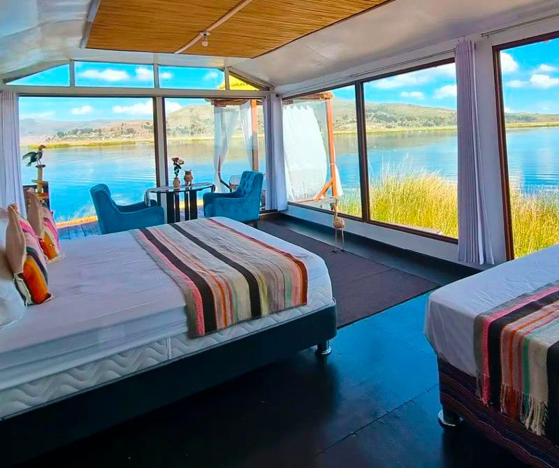 Habitación Matrimonial Panorámica con cama, sillones azules y ventanales hacia el Lago Titicaca